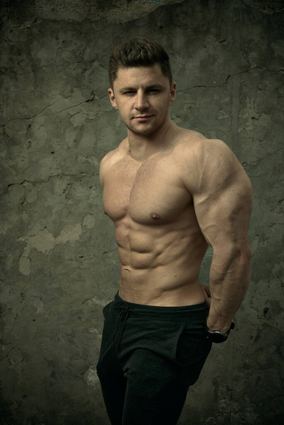 Schöner muskulöser Mann, der auf Betonwänden posiert. Das Konzept von Fitness, Bodybuilding, Gesundheit, Lebensstil. Fitnessmodel im Porträt. - Foto, Bild