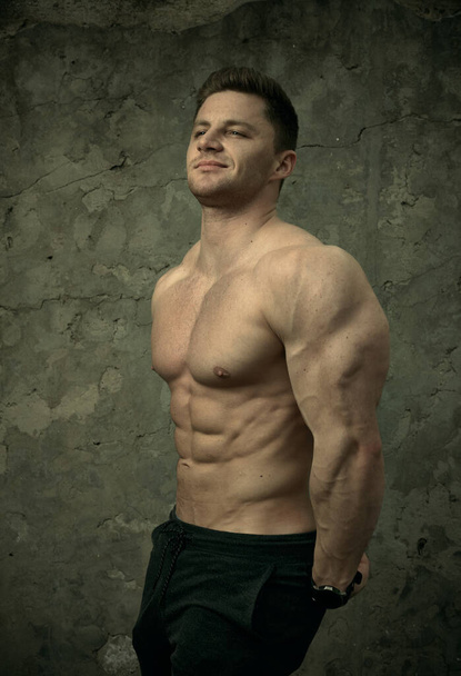 Hombre musculoso guapo posando sobre fondo de pared de hormigón. El concepto de fitness, culturismo, salud, estilo de vida. Retrato del modelo fitness
. - Foto, Imagen