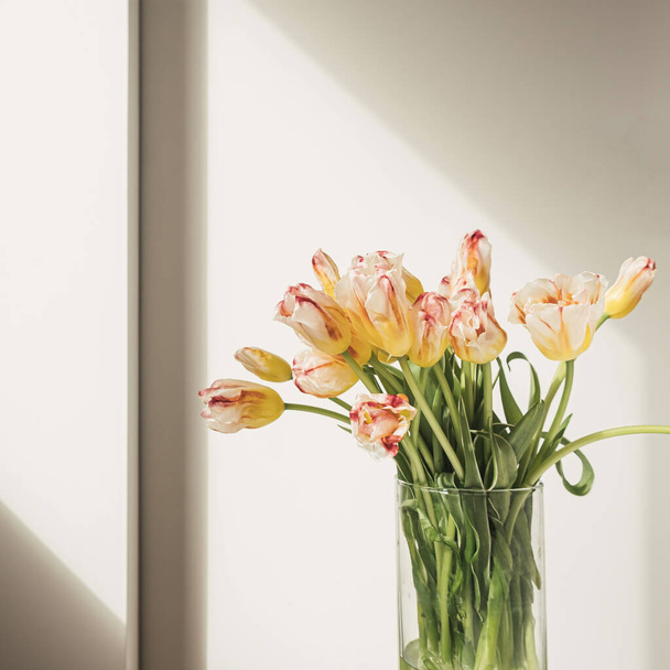 Yellow tulip flowers bouquet in glass vase against the white wall. Holiday celebration concept. Interior decoration. - Fotó, kép
