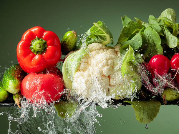 Διάφορα ωμά λαχανικά με νερό. Κουνουπίδι, ντομάτα, αγγούρι, ραπανάκι και πάπρικα σε πράσινο φόντο. - Φωτογραφία, εικόνα