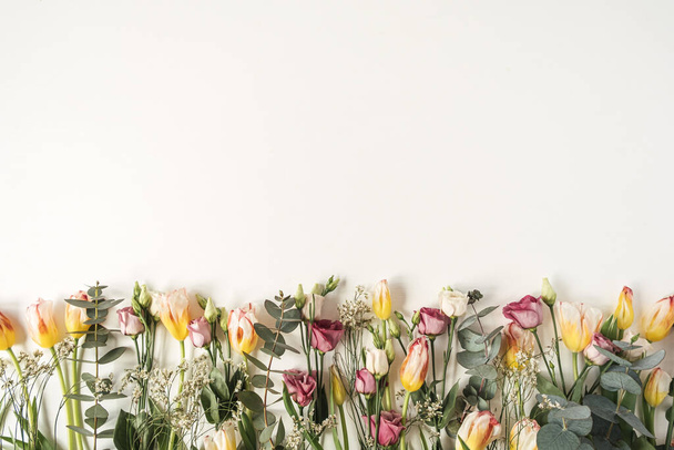 Květinová kompozice s mnoha tulipány, eukalypty, divoké květiny na bílém pozadí. Flat lay, top view slavnostní sváteční oslava hrdina záhlaví - Fotografie, Obrázek