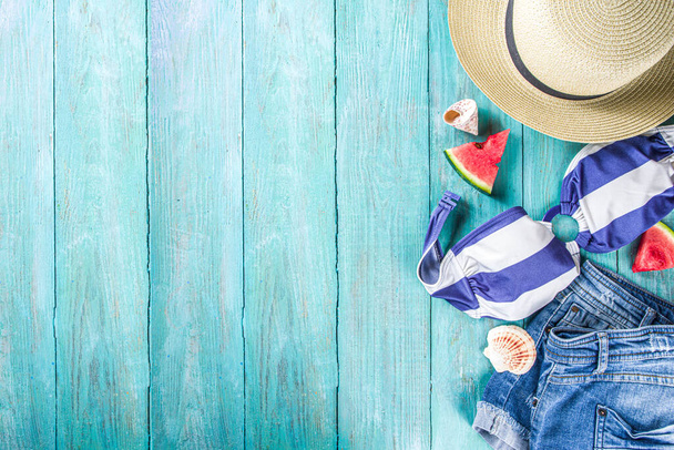 Summer holiday vacation concept. Summer vacation at sea. Female swimsuit, shorts and a straw hat, with slices of watermelon and seashells on a blue wooden background. Top view mock up copy space - Photo, Image
