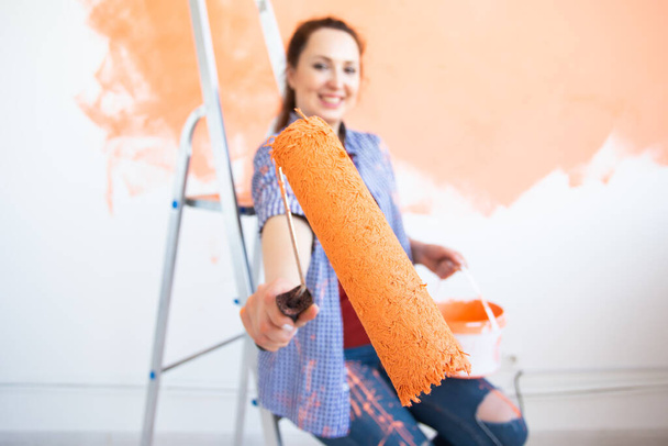 Yeni evdeki boya silindiriyle iç duvarı boyayan komik bir genç kadın. Duvara boya süren tekerlekli sandalyeli bir kadın.. - Fotoğraf, Görsel