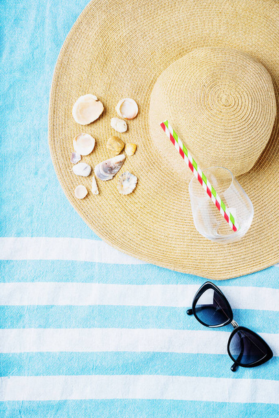 Summertime concept. Beach set: sunglasses, shells, glass with straws and summer hat on the striped beach towel. Top view. - Photo, Image