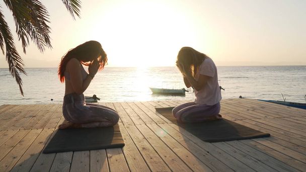 夕暮れ時に海辺で瞑想する二人の女性のシルエット - 写真・画像