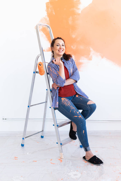 Щаслива усміхнена жінка малює внутрішню стіну нового будинку. Реконструкція, ремонт, ремонт квартир та концепція відпочинку
. - Фото, зображення