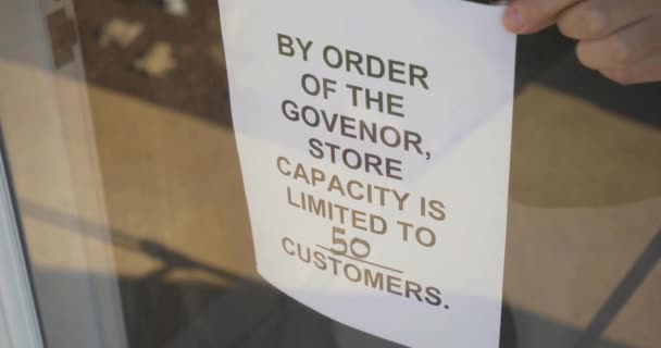 Een winkelier zet een COVID-19 waarschuwingsbord op de voordeur beperkte klanten. Tijdens de coronaviruspandemie van 2020 was vaak capaciteitsvermindering nodig voor bedrijven..   - Video