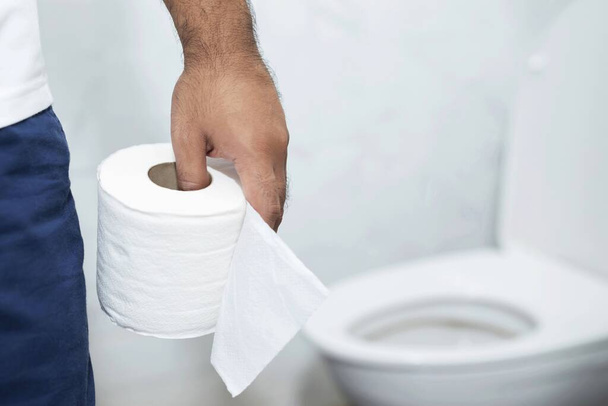 άνθρωπος πάσχει από διάρροια κατέχει ρολό χαρτί υγείας μπροστά από λεκάνη τουαλέτας. Στομάχι - Φωτογραφία, εικόνα
