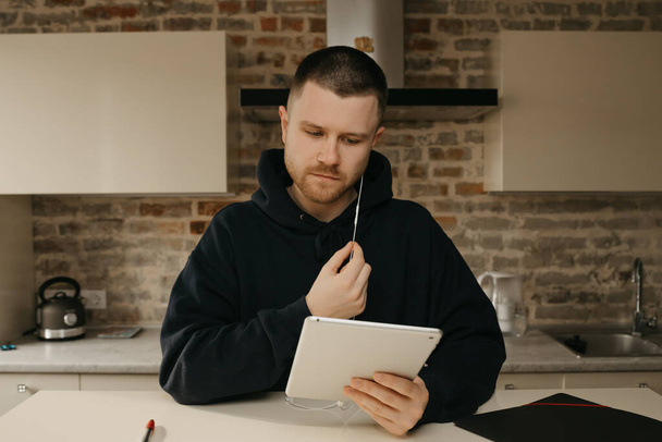 Studeren op afstand online. Een man met een baard die op afstand studeert op zijn tablet. Een kerel die naar een webinar kijkt.  - Foto, afbeelding