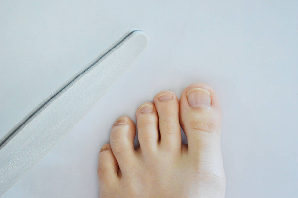 Pies femeninos piernas uñas lima en manos belleza pedicura sobre fondo blanco aislamiento. Spa en casa
 - Foto, imagen