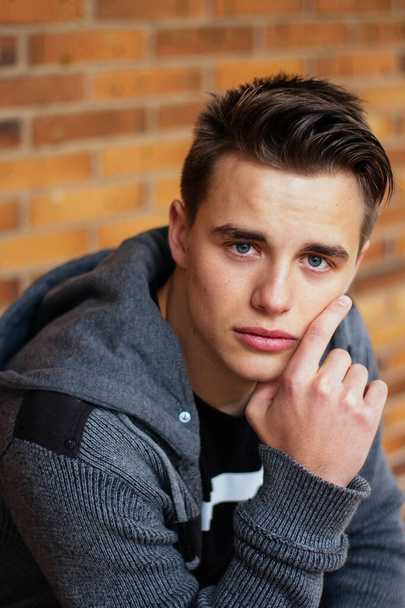 Portrait of young handsome man sitting with brick wall in the background - Photo, Image