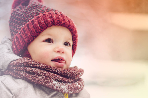 Funny little child girl wearing in red hat, a scarf, and a warm winter suit with gloves having fun at winter day in beautiful winter park playing with snow - Fotoğraf, Görsel