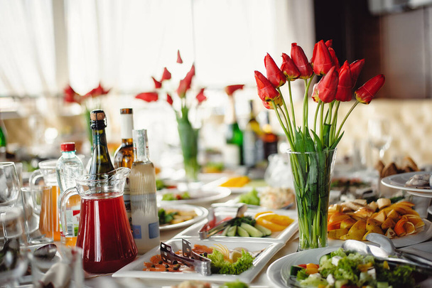 Served in a restaurant. Snacks, salads and a bunch of flowers of red tulips at the banquet table at the restaurant. Beautifully served banquet table with flowers and candles - Foto, imagen