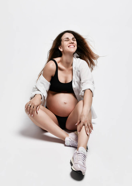 Portrait of a young brunette woman pregnant with happiness face smiling and lying on a light studio background with relaxing emotion. - Foto, immagini