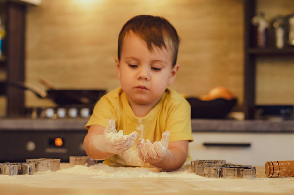 Sweet little cute child boy is learning how to make a cake, in the home kitchen. Concept of family leisure in the kitchen, child preparing food, various dishes: pasta, cookies, bread, gingerbreads. Vintage color tone.  - Photo, image