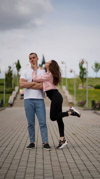 Young couple, man and woman in alley in park. Girl reaching for a pouted guy who turning away with offended expression - Foto, imagen