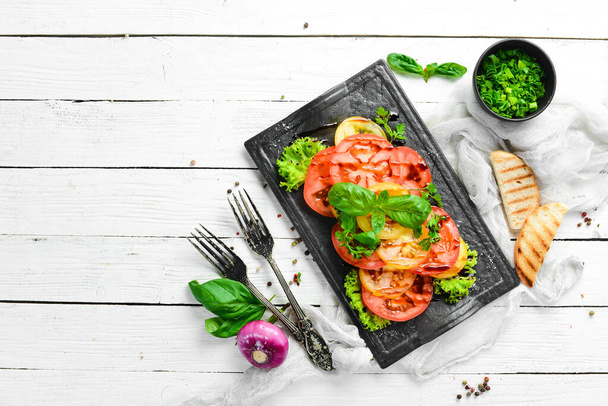 Salad of fresh tomatoes and basil on a black stone plate. Top view. Free copy space. - Foto, imagen