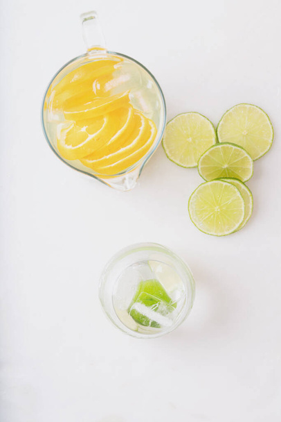 Homemade citrus infused water in a jug and in a glass with ice and slices of orange and lime isolated on a white background. Top view. - Photo, Image