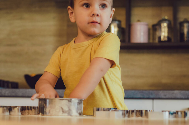 Sweet little cute child boy is learning how to make a cake, in the home kitchen. Concept of family leisure in the kitchen, child preparing food, various dishes: pasta, cookies, bread, gingerbreads. Vintage color tone.  - Foto, afbeelding