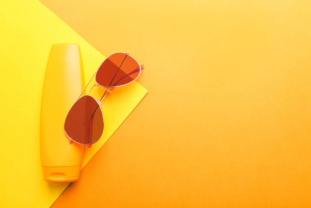 Opalovací krém a brýle na žlutooranžovém pozadí. Ochrana kůže. - Fotografie, Obrázek