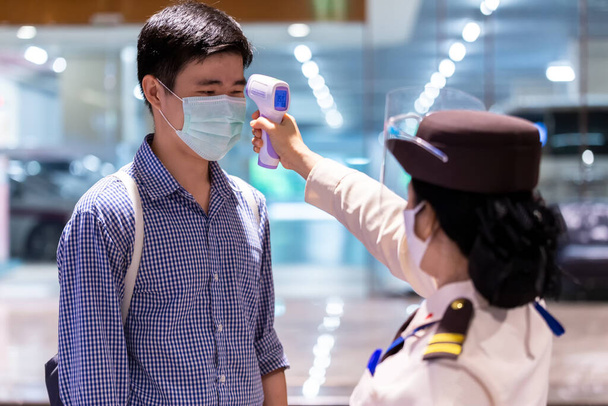 Gardien de sécurité utilisant un thermomètre infrarouge pour mesurer la température corporelle vérifier les personnes asiatiques dans le masque de protection médicale avant l'accès à l'immeuble de bureaux pour lutter contre la grippe épidémique Coronavirus (CoVID-19) de wuhan
. - Photo, image