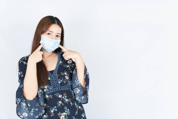 Азиатская красивая счастливая женщина хипстер носить медицинскую защиту лица маску для защиты коронавируса, фильтр пыли PM 2.5 и холодный и ее палец на маске на белом фоне
 - Фото, изображение
