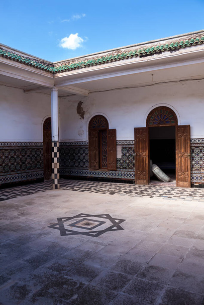 Parte bien conservada de un complejo abandonado. Patio con pavimentación, azulejos florales tradicionales en las paredes y puerta de madera abierta. Dar Caid Hadji (utilizado también Hajji), Marruecos
. - Foto, Imagen
