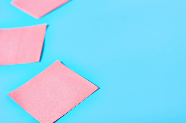 Row of pink square blank paper stickers on blue background. Copy space - Zdjęcie, obraz