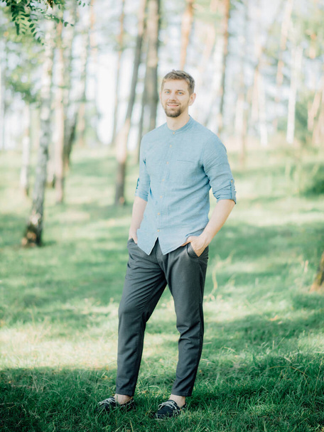 Stylish bearded man with blond hair dressed in a blue shirt posing for a photo in the park. - Φωτογραφία, εικόνα