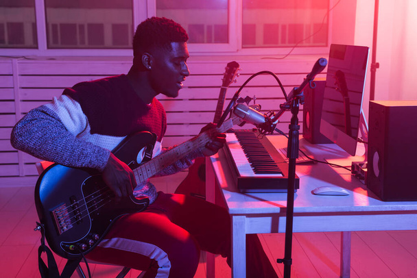 Αφροαμερικανός επαγγελματίας μουσικός ηχογράφησης μπάσο κιθάρα στο ψηφιακό στούντιο στο σπίτι, μουσική παραγωγή έννοια της τεχνολογίας. - Φωτογραφία, εικόνα