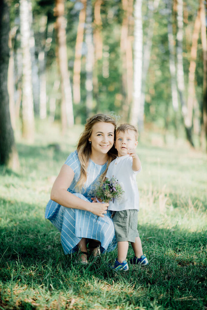 mother holding her son at a photo shoot to help him right pose for the photographer. Happy young family  outside in green nature - Φωτογραφία, εικόνα
