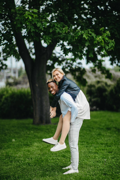 Mladý mezirasový pár má zábavu, hraje a směje se v parku. Koncept milostných vztahů a jednoty mezi různými lidskými rasami. - Fotografie, Obrázek