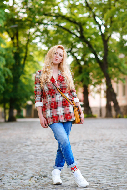 Hipster girl with long blonde hair wearing trendy plaid jacket posing at street. Urban clothing style. Women fashion, outfit. Outdoor lifestyle portrait of young girl. Fashion, lifestyle and people. - Photo, Image