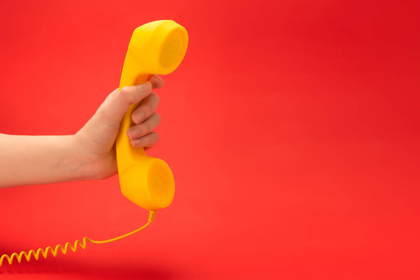 Желтый телефон на красном фоне в женской руке. Копирование пространства. - Фото, изображение