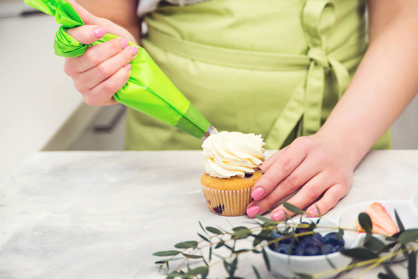 Female hands holding piping bag filled with cream cheese and decorating cupcakes. Pastry chef using a pastry bag. Desserts. Homemade pastry. Woman cooking cakes. - Valokuva, kuva