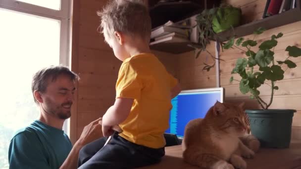 Baba evden çalışır ve küçük çocuğa su verir, kedi oturur ve yanında oynar, ebeveynlik çoklu görev anlayışı, tek başına yaşam tarzı iş yeri kavramı, salgın karantinasında kalmak - Video, Çekim