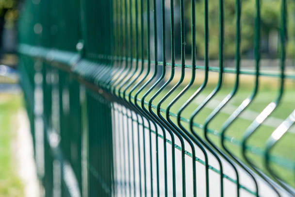 Χαλύβδινος φράχτης του γηπέδου ποδοσφαίρου, μεταλλικό σύρμα φράχτη με γρασίδι στο παρασκήνιο. - Φωτογραφία, εικόνα