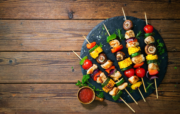 Chicken kebabs on skewers with mushrooms and vegetables on slate plate - Photo, image