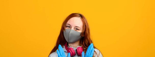 Portrait of a girl in a mask, which puts on a rubber glove. Yellow background, coronavirus pandemic. - Zdjęcie, obraz