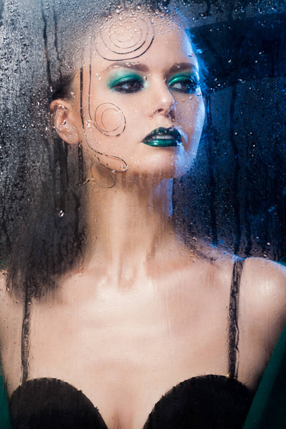 Beautiful model girl stands behind a glass with raindrops. - Φωτογραφία, εικόνα