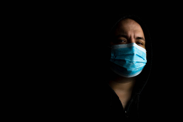 Καυκάσιος νεαρός άνδρας με ιατρική προστατευτική μάσκα προσώπου απεικονίζει πανδημικό coronavirus, νόσος Covid 19 απομονωμένη σε μαύρο χώρο αντιγραφής. Εξάνθημα Covid-19, μόλυνση γρίπης και έννοια της υγειονομικής περίθαλψης - Φωτογραφία, εικόνα