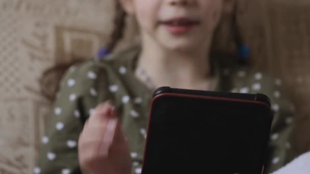 Κοριτσάκι που διαβάζει ηλεκτρονικό βιβλίο στον καναπέ στο σπίτι - Πλάνα, βίντεο