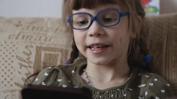 Little girl reading electronic book on couch at home - Imágenes, Vídeo