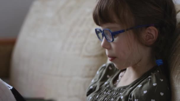 Petite fille lisant le livre électronique sur le canapé à la maison
 - Séquence, vidéo