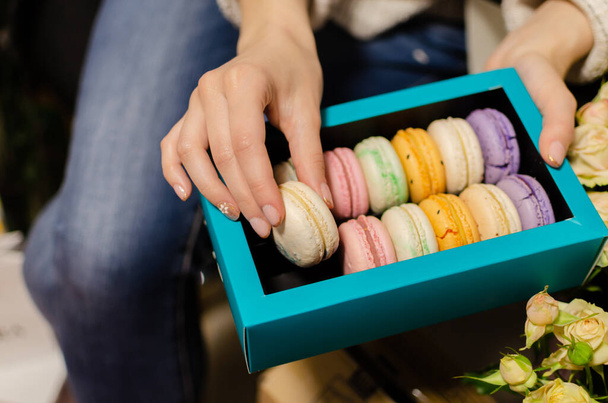 mano femenina con galletas de macarrones francés dulce y colorido, postre en una caja, primer plano
 - Foto, Imagen