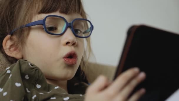 Κοριτσάκι που διαβάζει ηλεκτρονικό βιβλίο στον καναπέ στο σπίτι - Πλάνα, βίντεο