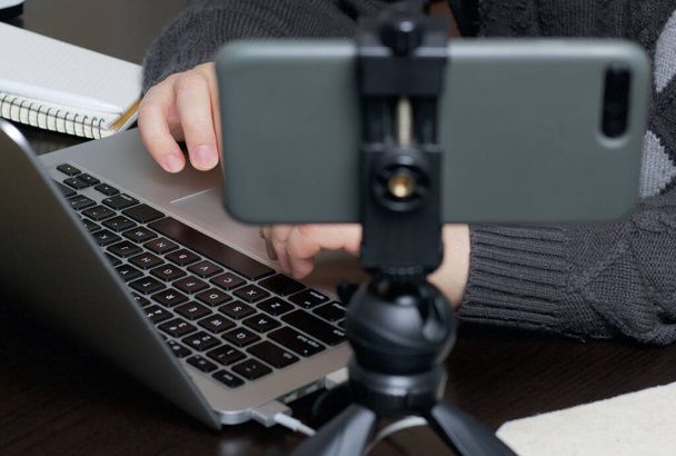 A man works at a laptop. Near the smartphone on a tripod. Hands are taken close up. - 写真・画像