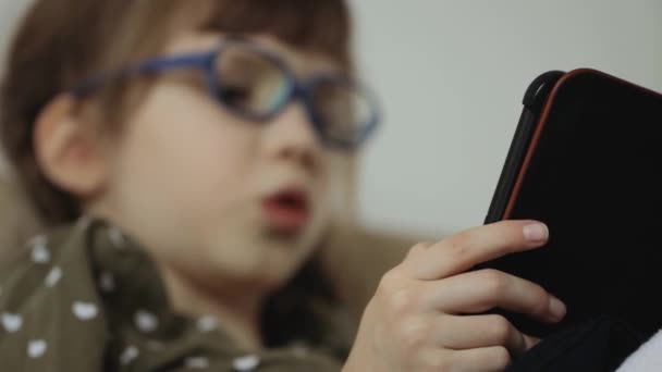 Little girl reading electronic book on couch at home - Footage, Video