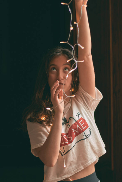 Дівчина в темряві з світлодіодними вогнями в руках з білою футболкою і довгим коричневим волоссям з руками вгору
 - Фото, зображення