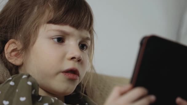 Little girl reading electronic book on couch at home - Footage, Video